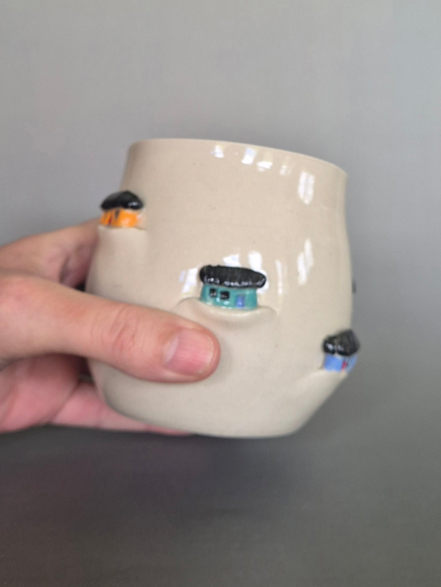 Hand holding a ceramic vase with decorative elements on a gray background