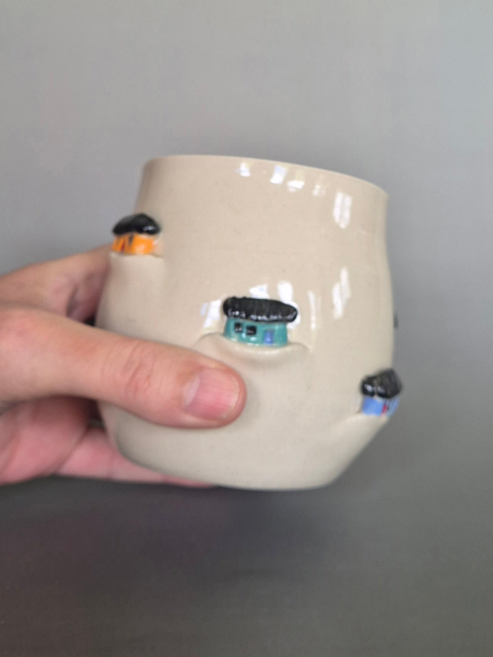 Hand holding a ceramic vase with decorative elements on a gray background