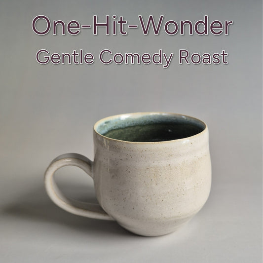 Ceramic mug on a gray background with text 'One-Hit-Wonder Gentle Comedy Roast'.