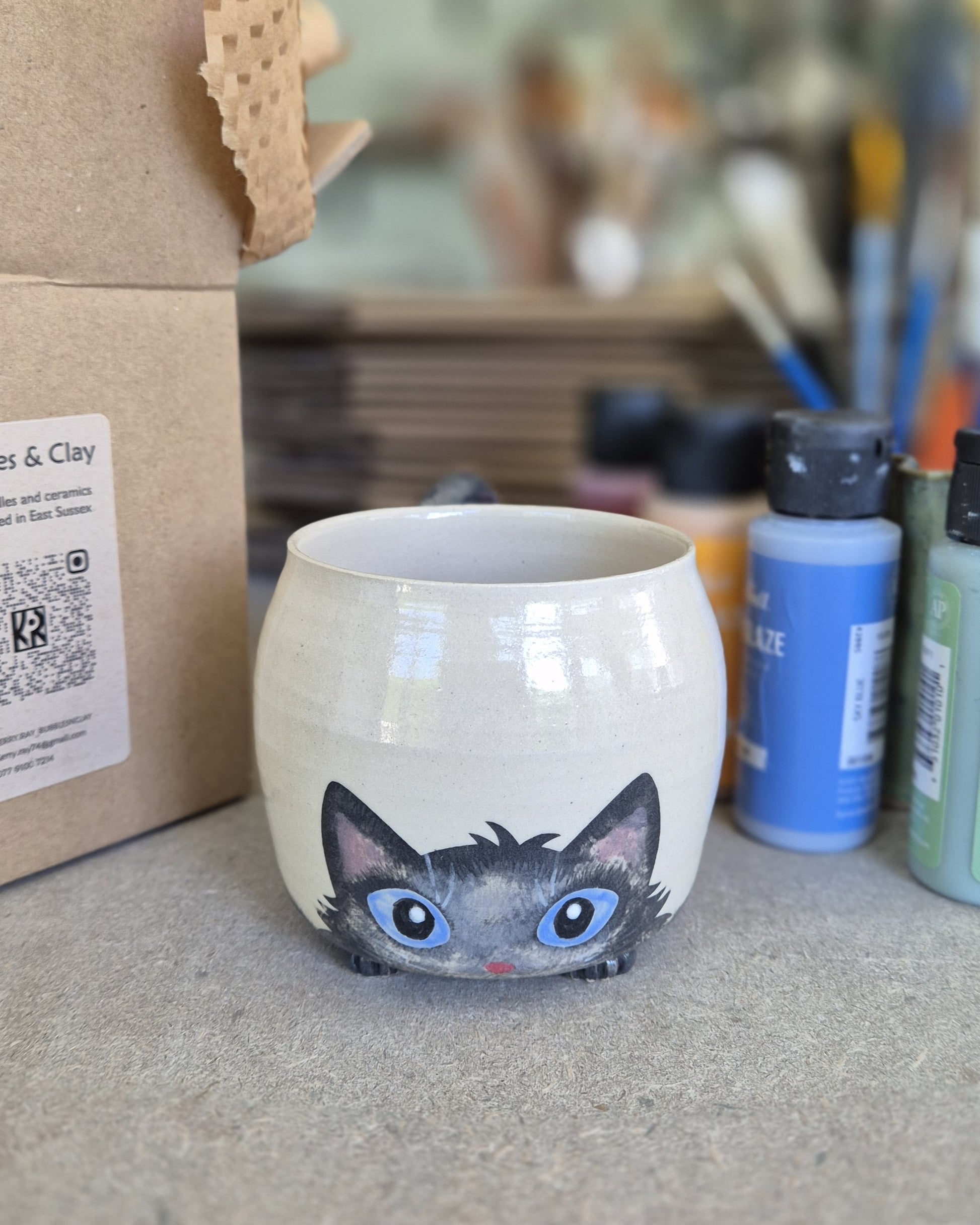 Ceramic mug with a cat design on a surface with art supplies in the background