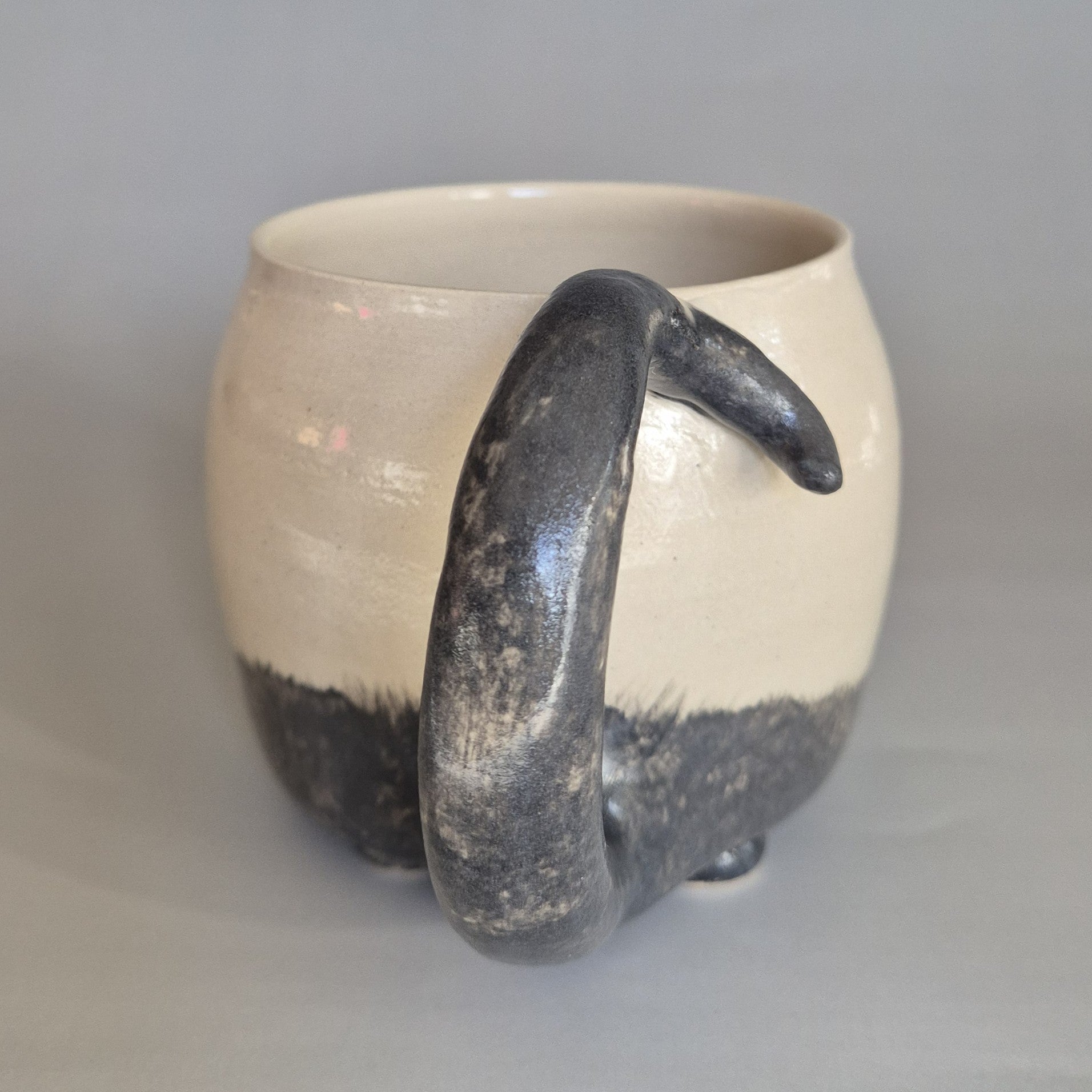 Ceramic cat mug with a black tail handle on a gray background