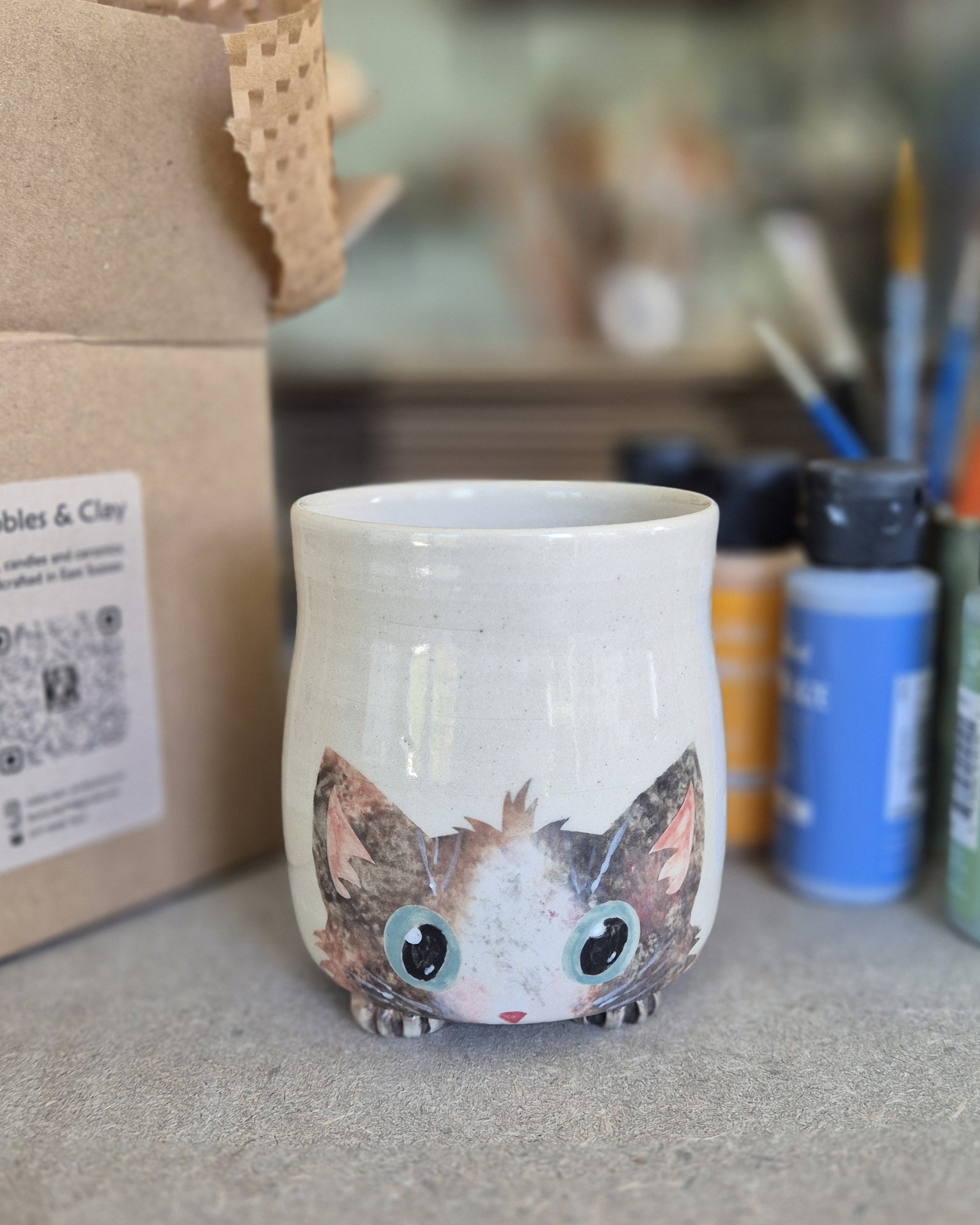Ceramic mug with a cat design on a surface with art supplies in the background