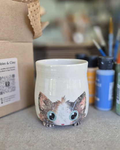 Ceramic mug with a cat design on a surface with art supplies in the background