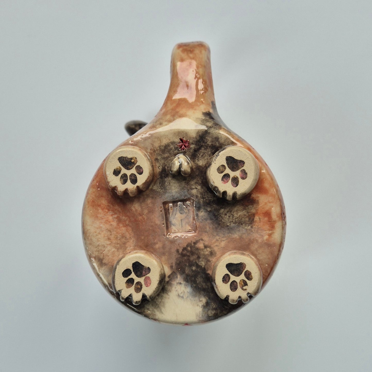Base of a ceramic cat mug showing paws and other details. On a gray background