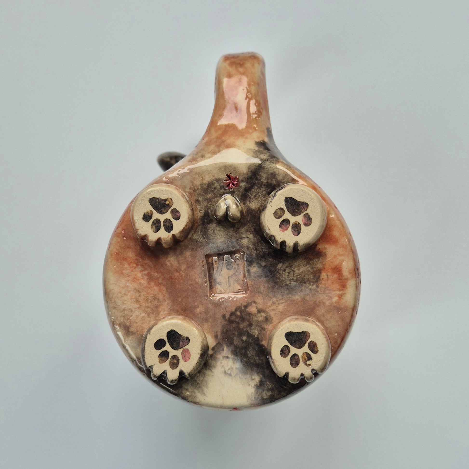 Base of a ceramic cat mug showing paws and other details. On a gray background