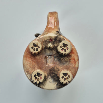 Base of a ceramic cat mug showing paws and other details. On a gray background