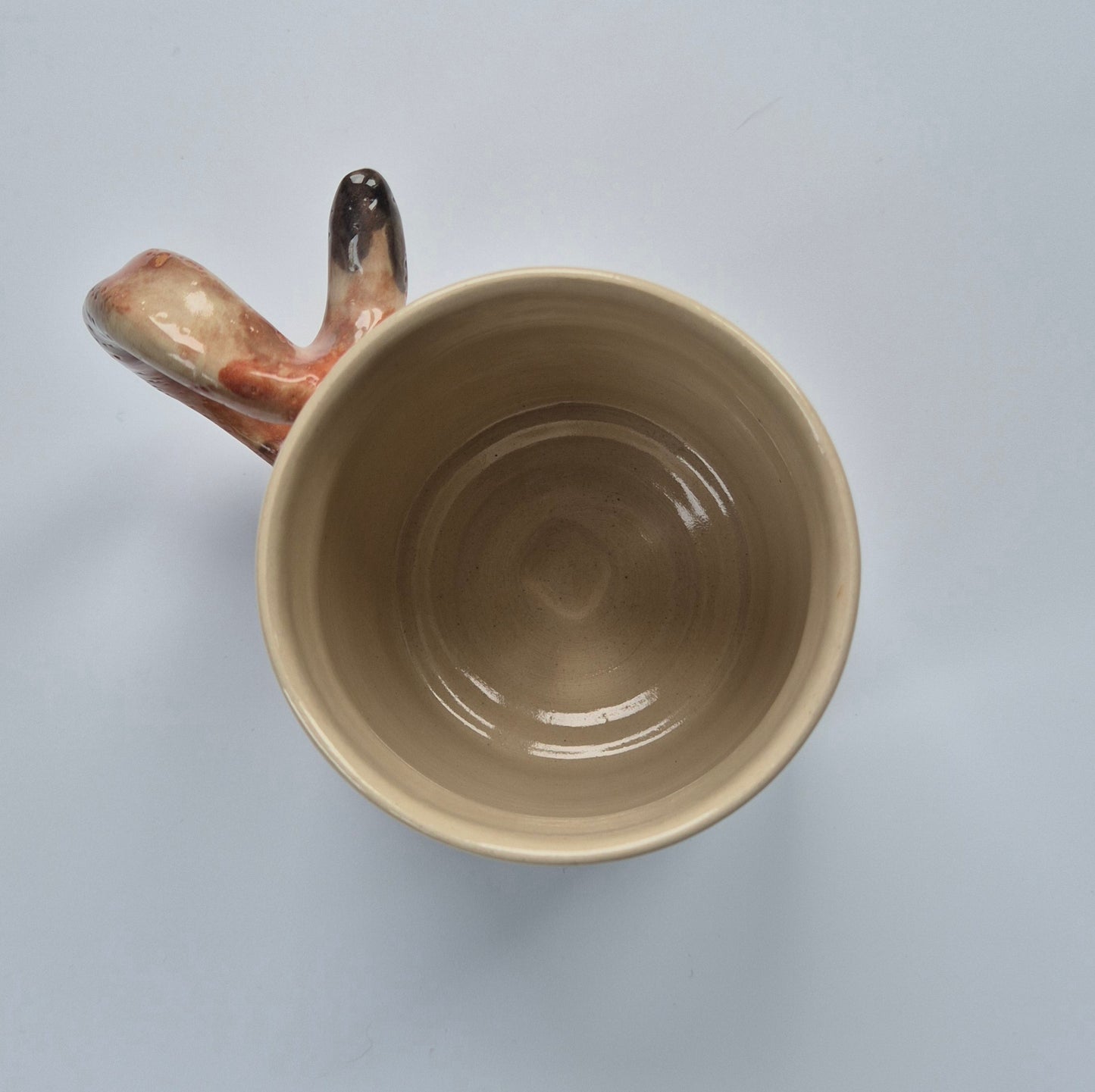 Inside of a Beige ceramic cat mug with a unique handle on a light gray background