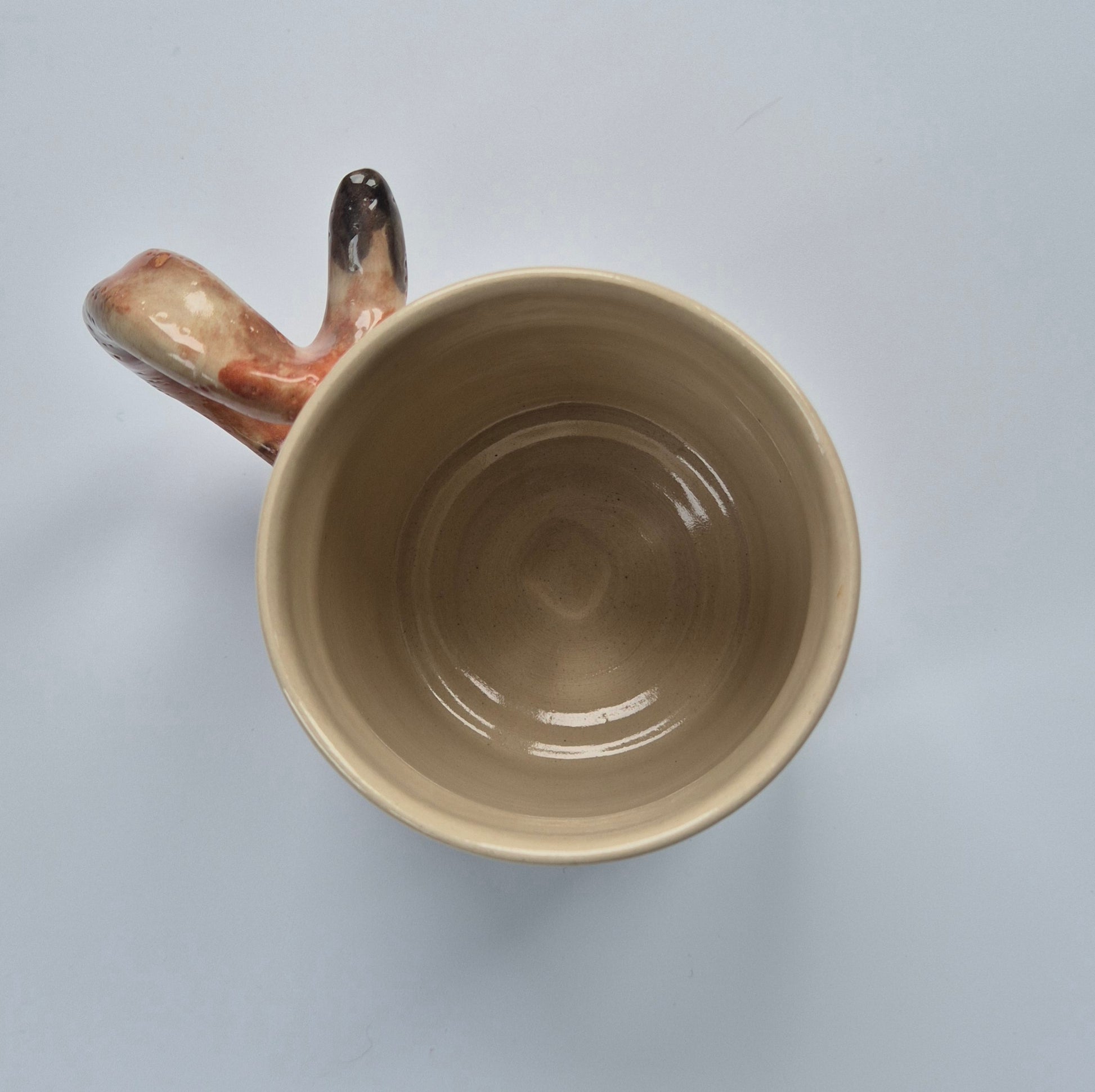 Inside of a Beige ceramic cat mug with a unique handle on a light gray background