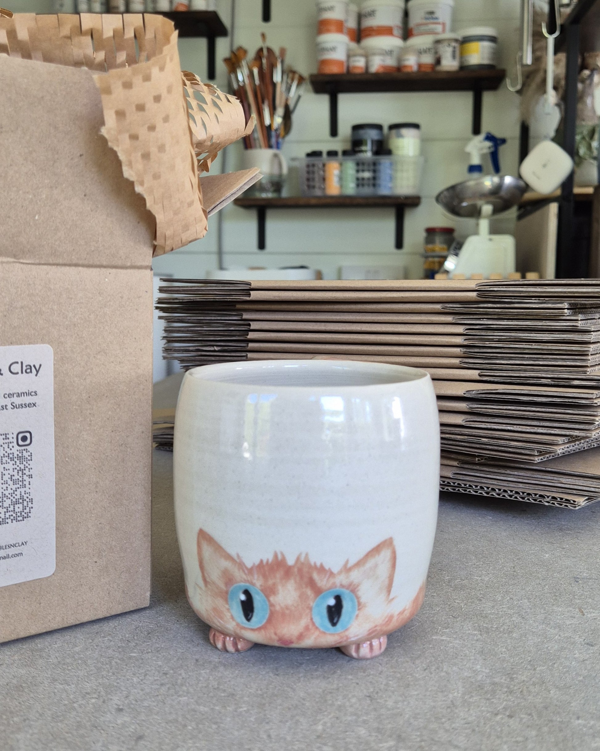 Cat-shaped ceramic mug on a surface with stacks of paper and supplies in the background