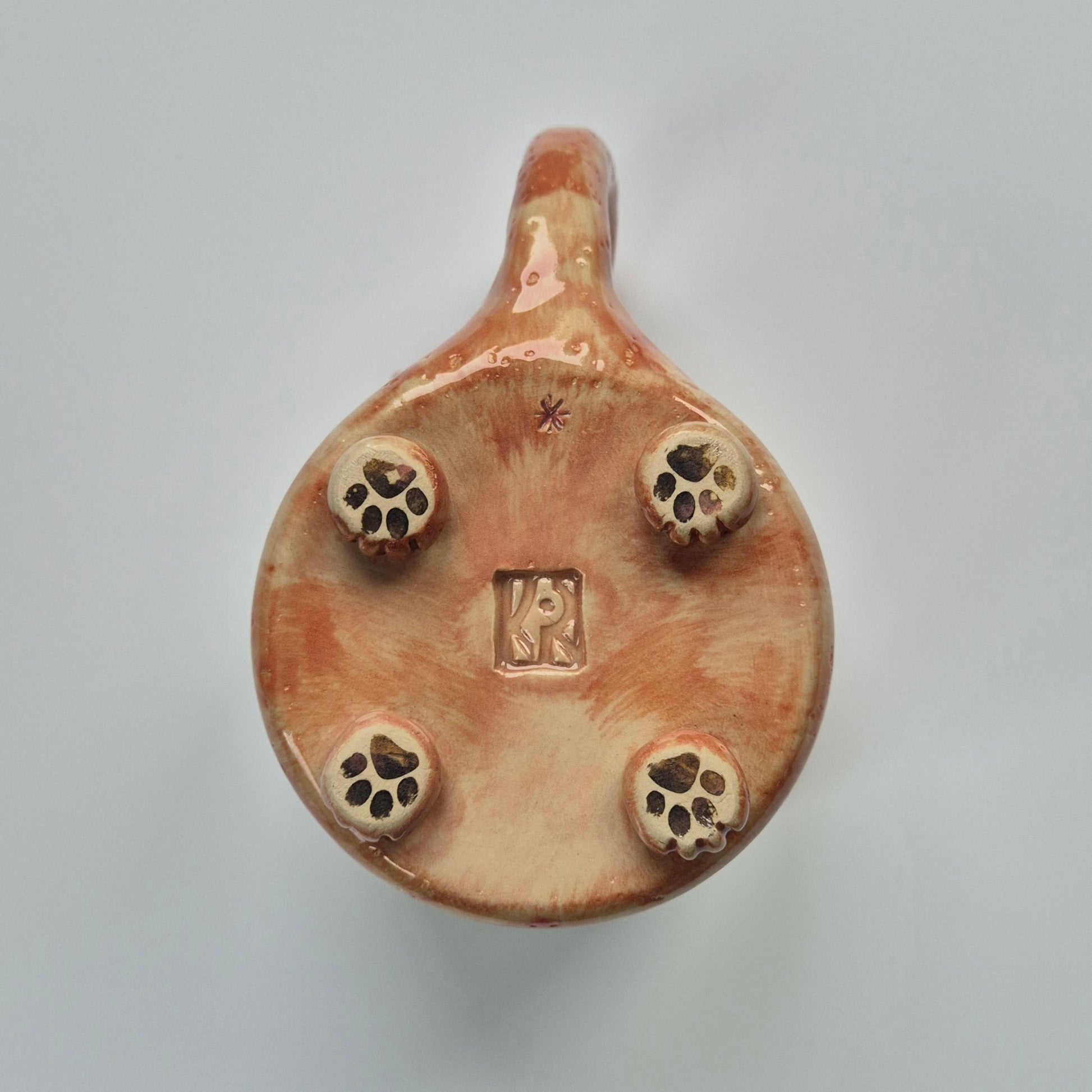 base of a ceramic cat mug showing details of paws on a plain background