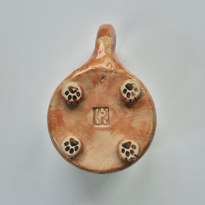 base of a ceramic cat mug showing details of paws on a plain background