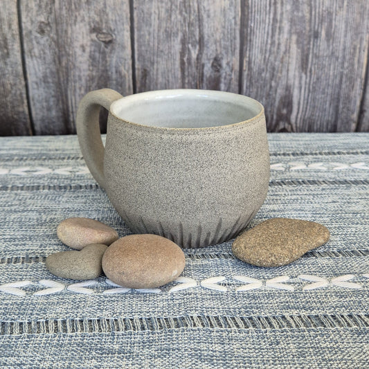Ceramic mug with textured surface on a textured fabric surface with stones.