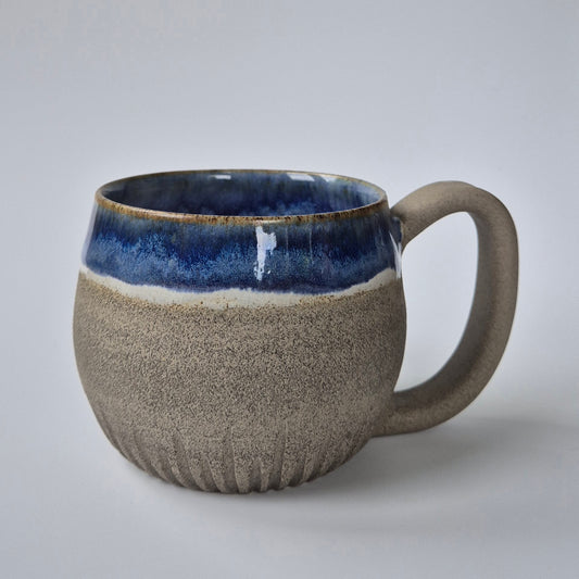 Ceramic mug with blue interior and textured beige exterior on a light gray background