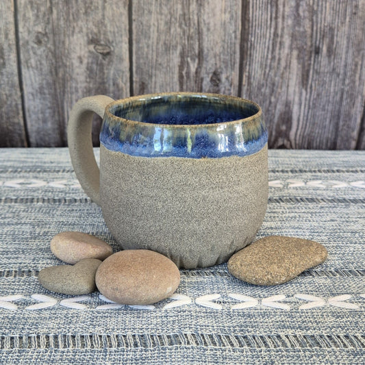 Ceramic mug with blue interior on a textured surface with stones
