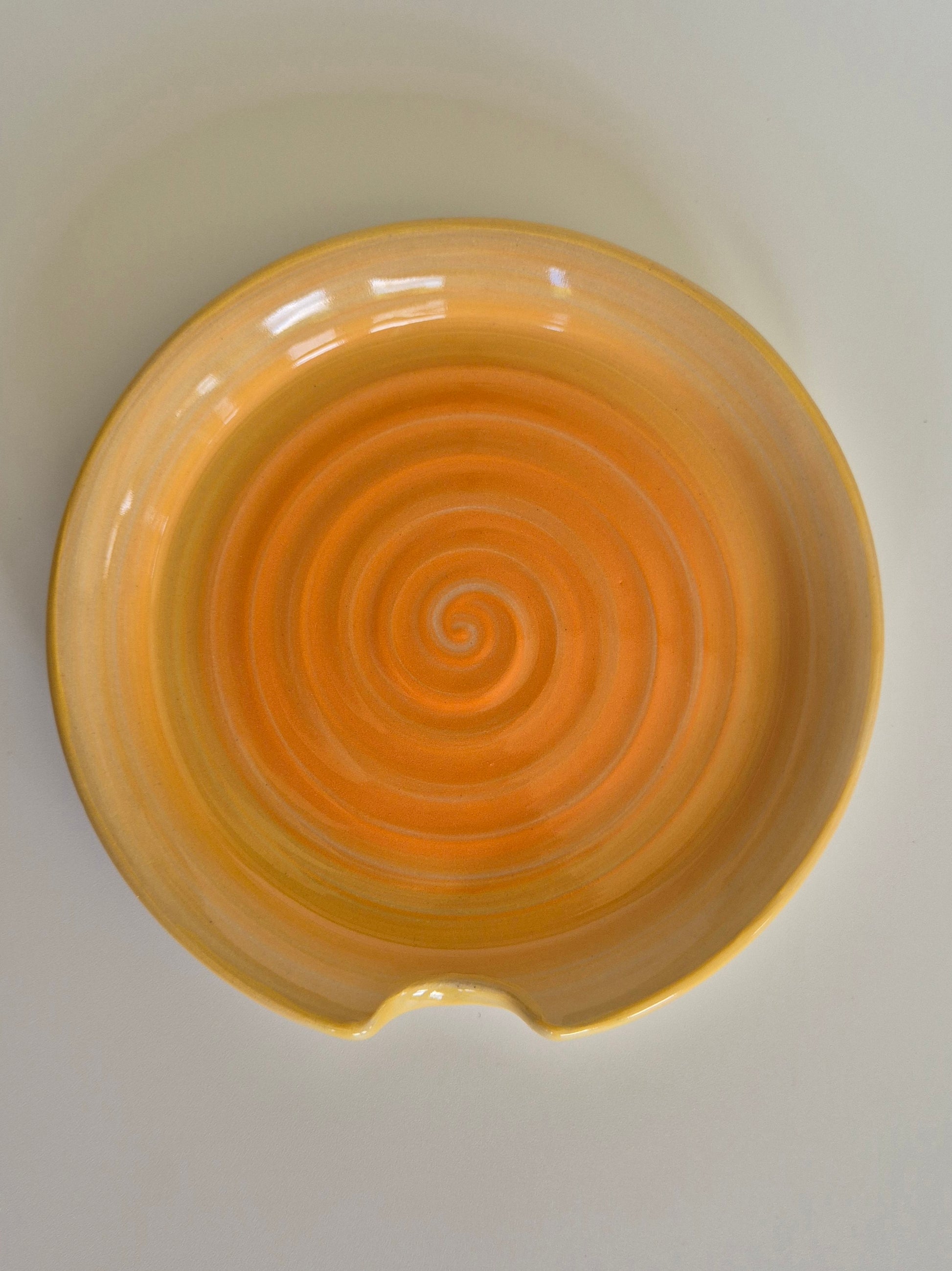 Yellow ceramic spoon rest with a spiral design on a white background