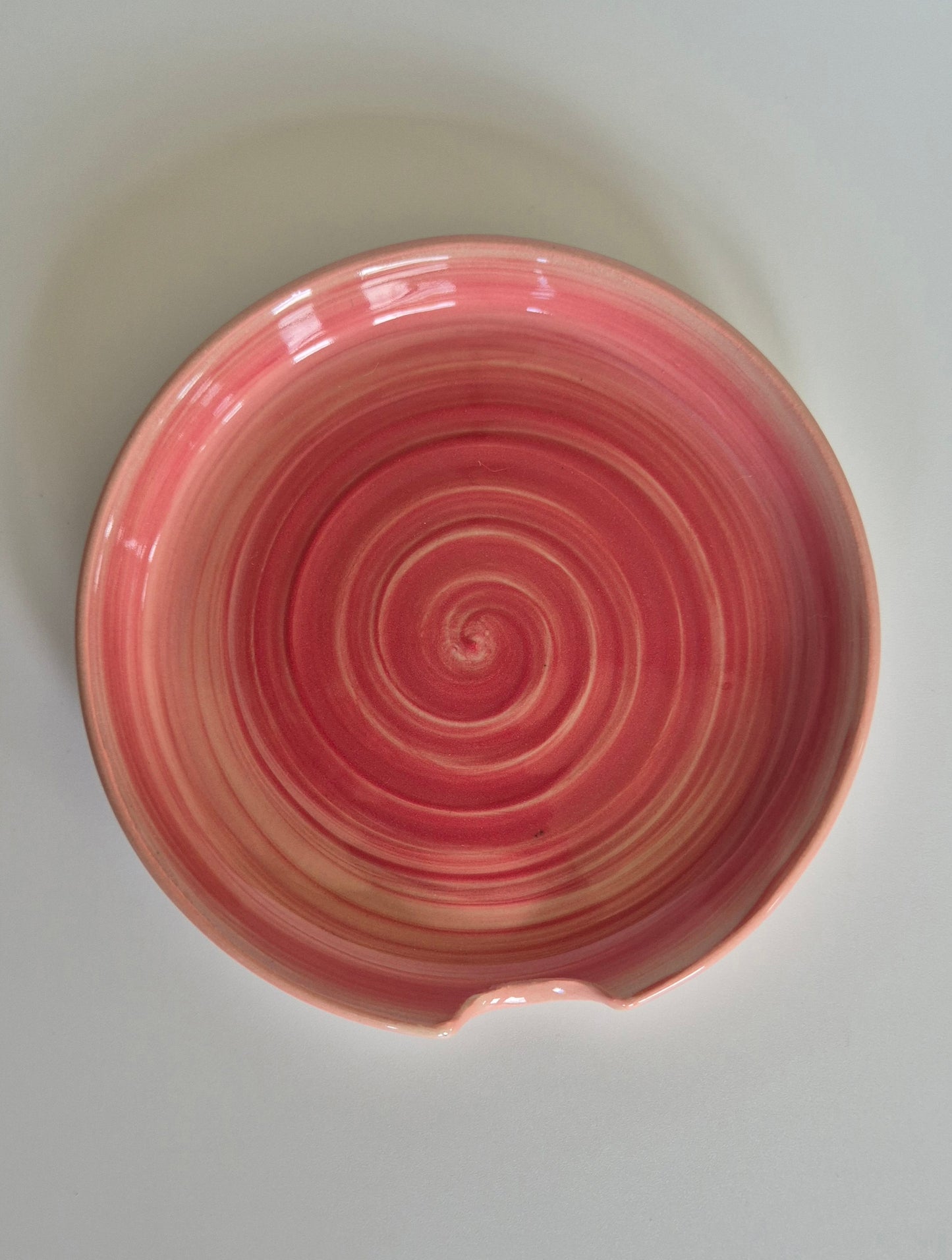 Pink ceramic spoon rest with a spiral pattern on a white background