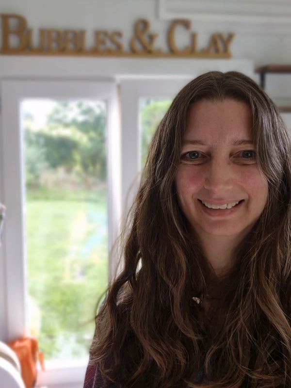 Kerry in her studio - smiling in front of a window with 'Bubbles & Clay' sign above.